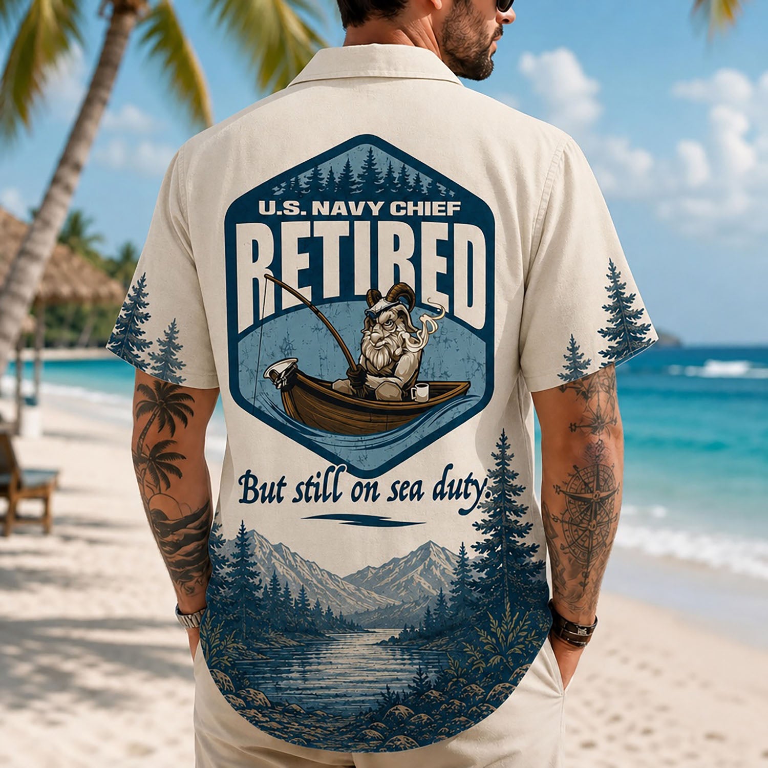 Back view lifestyle of a man on a beach wearing the custom veteran retirement shirt showing the large fishing GOAT emblem print and mountains