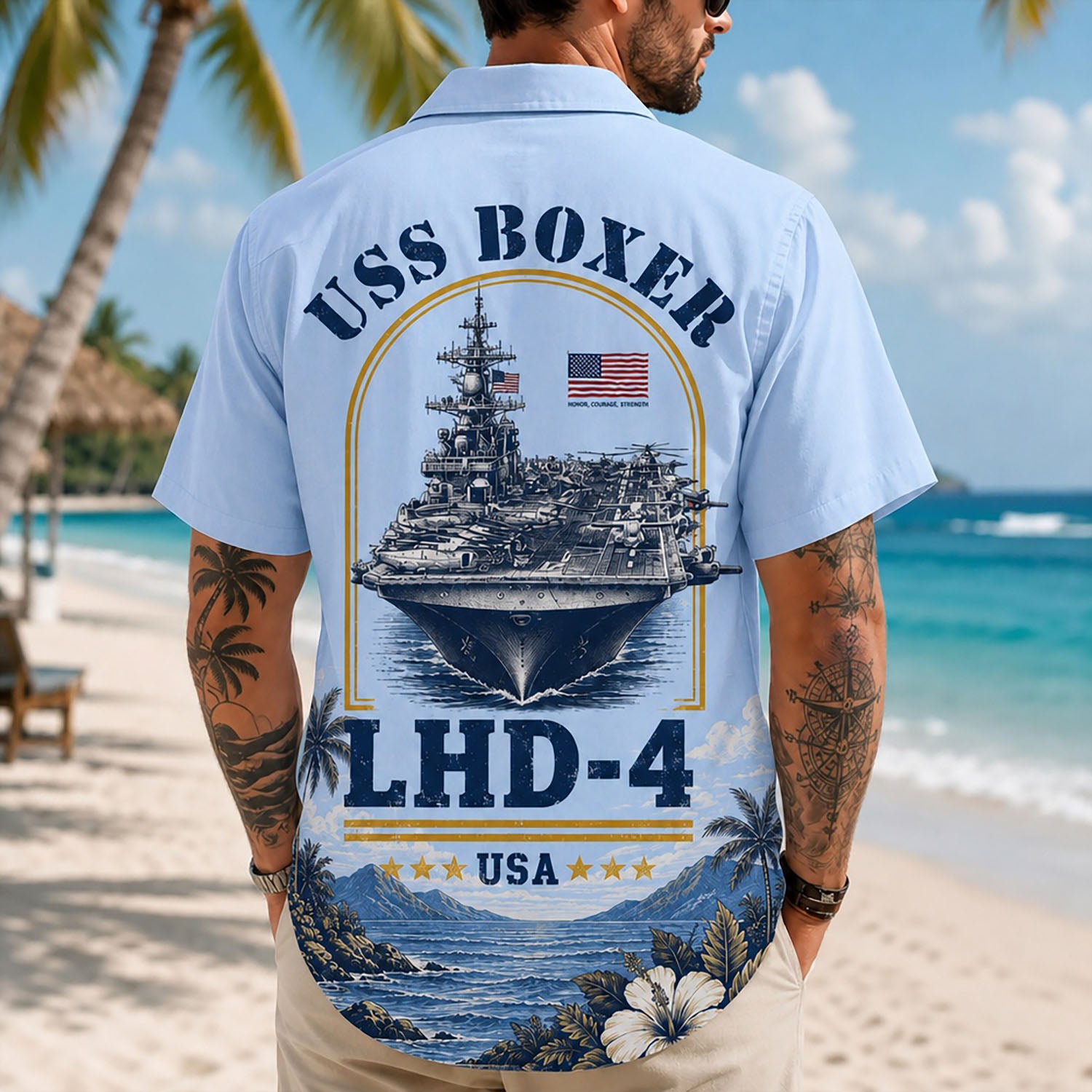 Back view lifestyle of a male model on a beach wearing the light blue USS Boxer LHD-4 custom military shirt with detailed aircraft carrier artwork