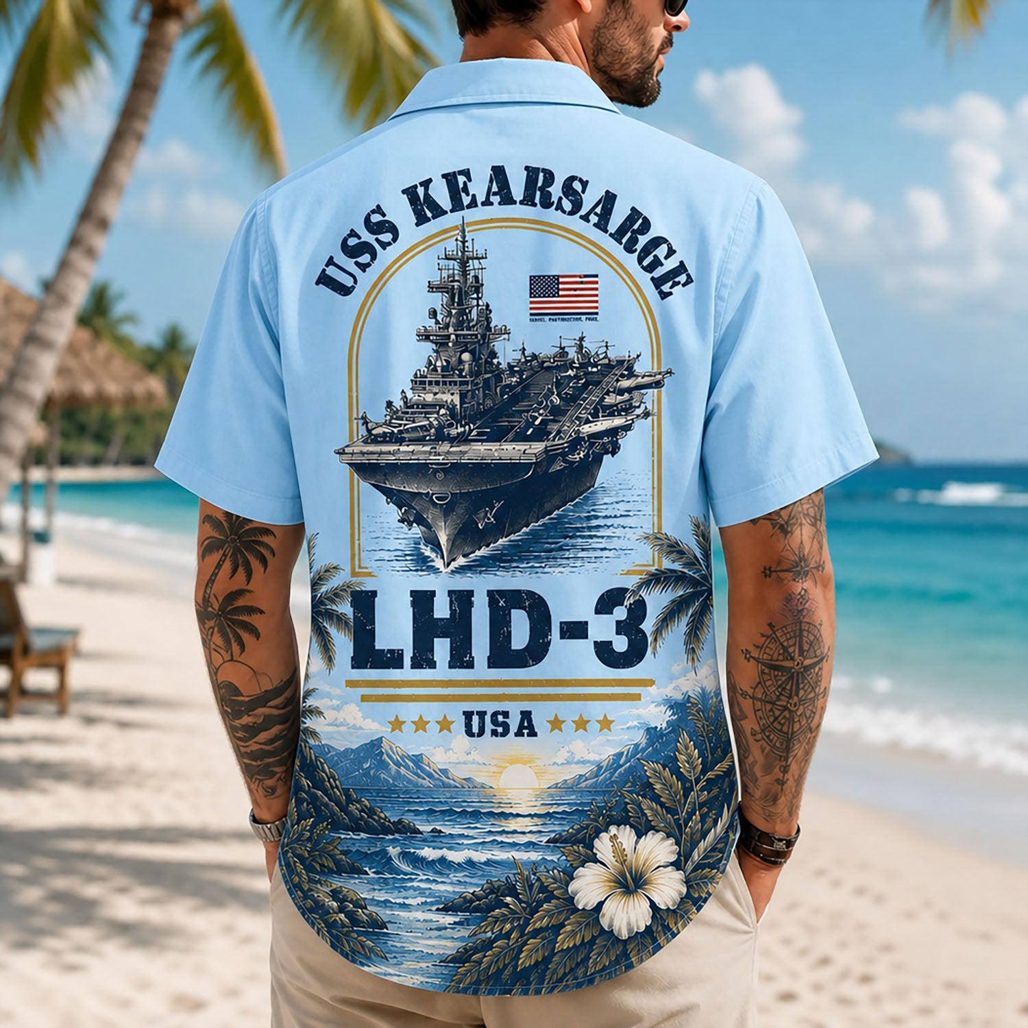 Back view lifestyle of a male model on a beach wearing the light blue USS Kearsarge LHD-3 custom military Hawaiian shirt with detailed ship artwork